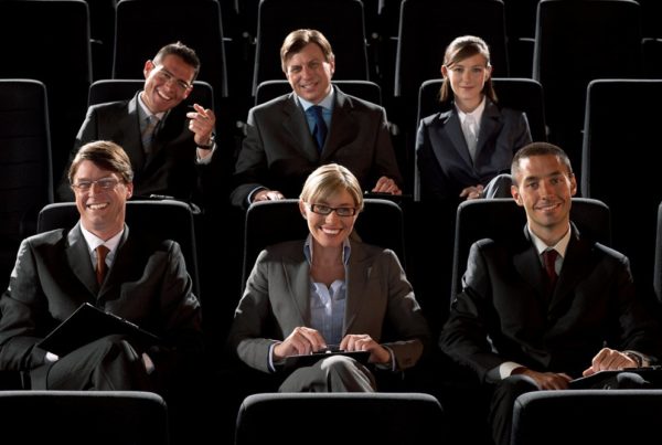 Image of Six businessmen and businesswomen in auditorium, smiling, portrait. Photo by Unknown/Canva.