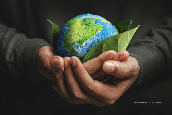 This is a stock photo by Monica Todica | Canva. It shows a man's hands cradling a miniature globe sitting in a bed of leaves. The photo is used as art to accompany a press release announcing the release of the ICCA & Destination Canada International Sustainability Survey.