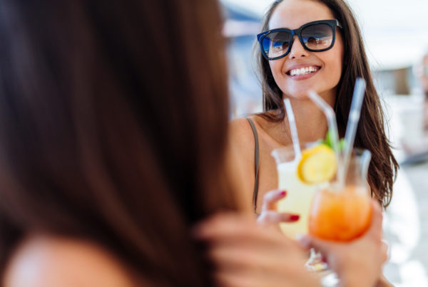Image of cheerful female friends drinking cocktails in summer and smiling. Photo by nd3000 | Canva.