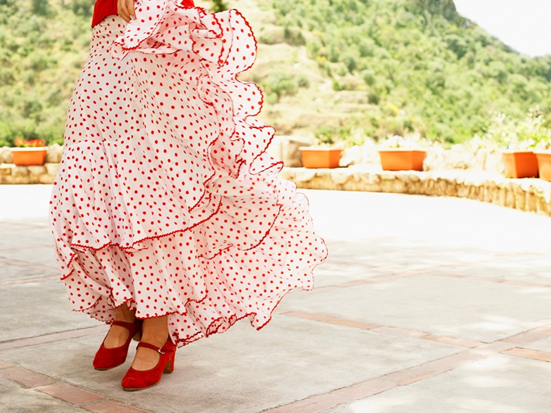 Image of a woman's flounced skirt and red shoes as she performs the flamenco in the outdoors. Photo by Lee | Canva.