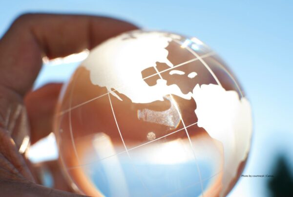 This stock image shows a man's fingers holding a glass globe with North and South American continents showing. Photo is by courtneyk | Canva.