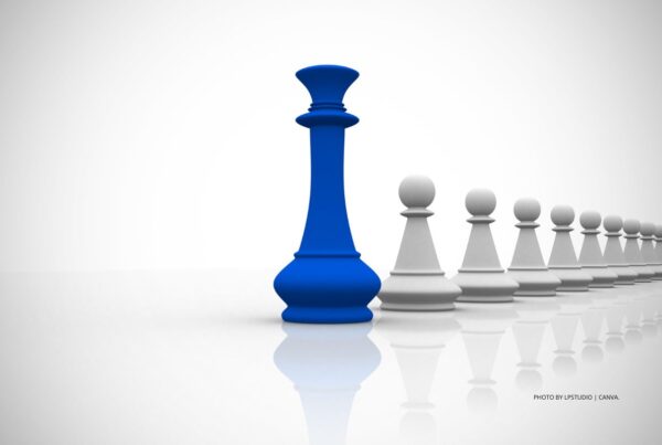 Leadership stock image by Lpstudio | Canva. This image shows a large, blue King chesspiece leading a row of white, pawn chesspieces. Photo is by Lpstudio | Canva.