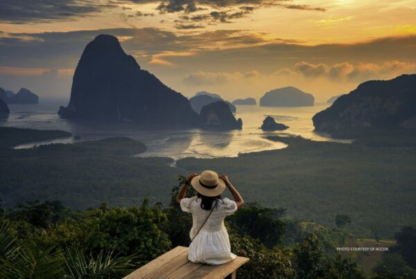 This is an image of a young woman wearing a hat and gauzy, white summer dress looking out over a scene with waters, and mountainous islands. It accompanies the press release from Accor about its new white paper: The Road Map Towards a Transformational Culture of Well-Being.