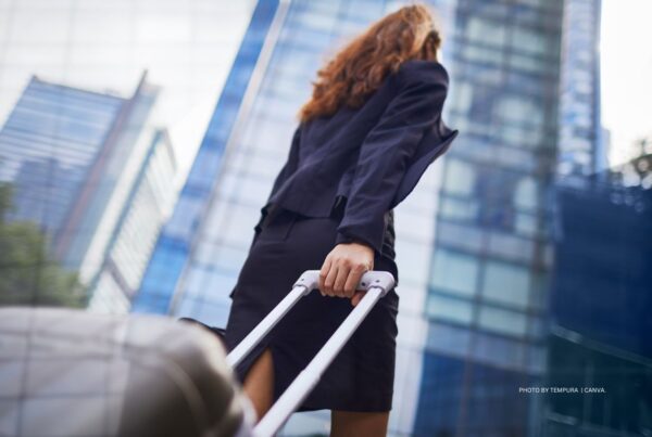 Business travel is expected to ramp up to pre-pandemic levels by the end of 2023, according to new research from GBTA and Spotnana. This image is a stock photo of a women in a business suit pulling a suitcase with city skyscrapers in background. Photo is by tempura | Canva.