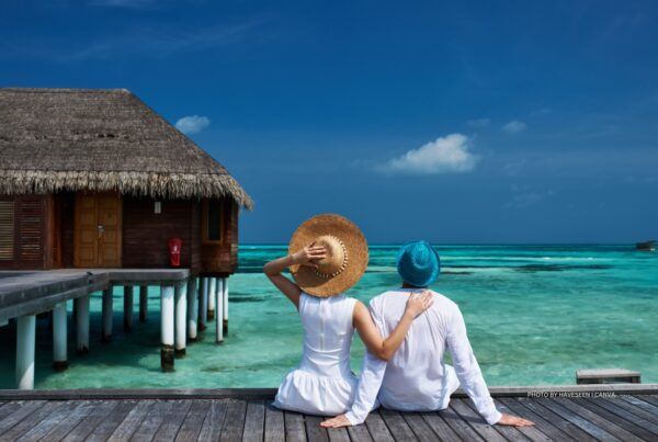 This is a stock image of a couple sitting on a jetty in The Maldives. Photo is by haveseen | Canva.