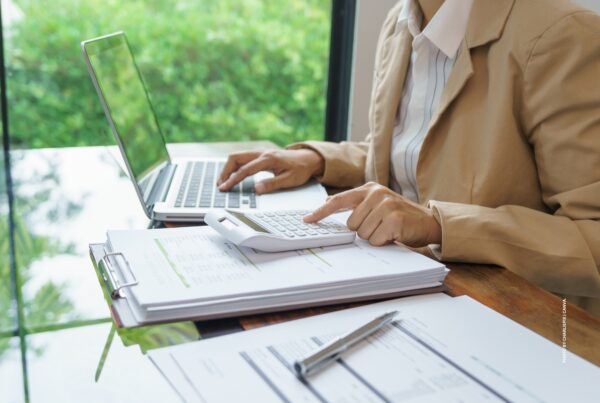This image is a stock image showing a woman sitting at a desk with a laptop, calculator and spreadsheets. Photo by charliepix | Canva.