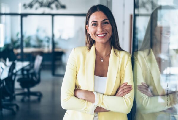 This is a stock image of a confident, optimistic young businesswoman with an office in the background. Photo by filadendron | Canva.
