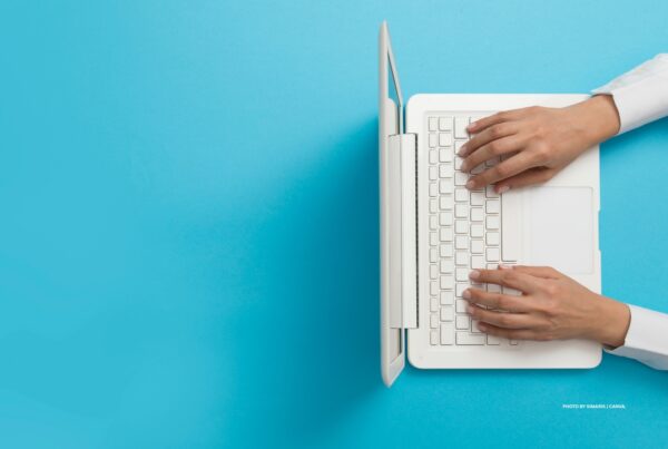 This is a stock photo of a woman working at a white laptop against bright turquoise background. Photo by simarik | Canva.